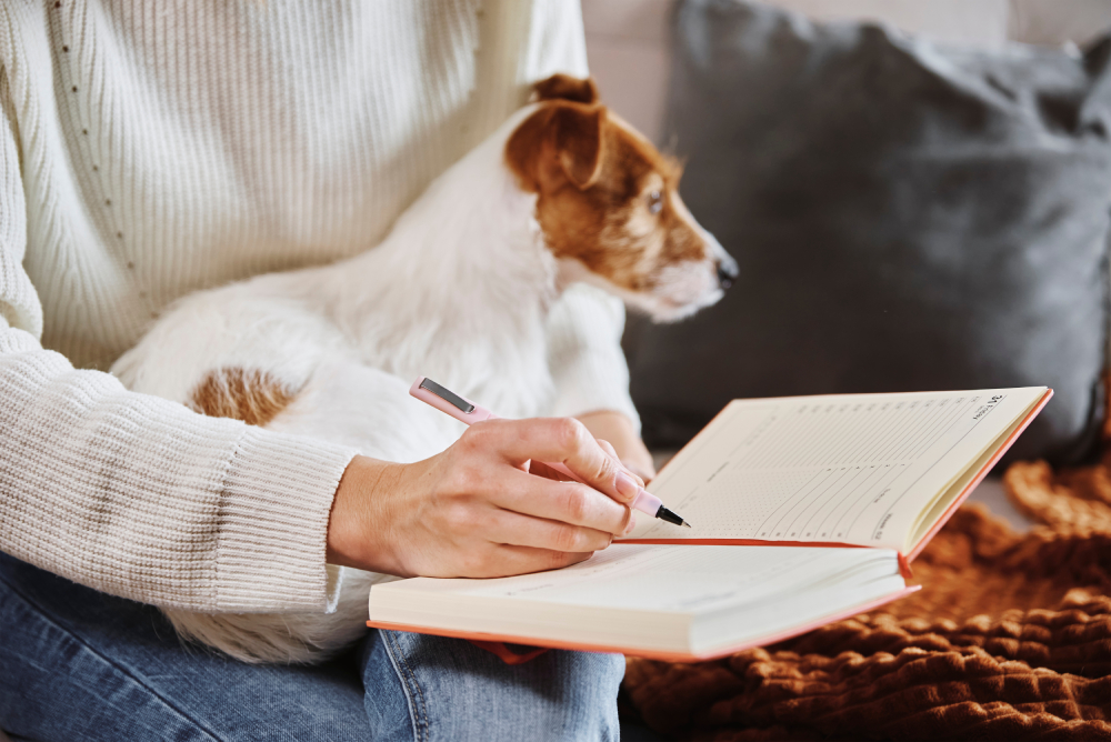 Woman working write notes in notebook at home with her dog