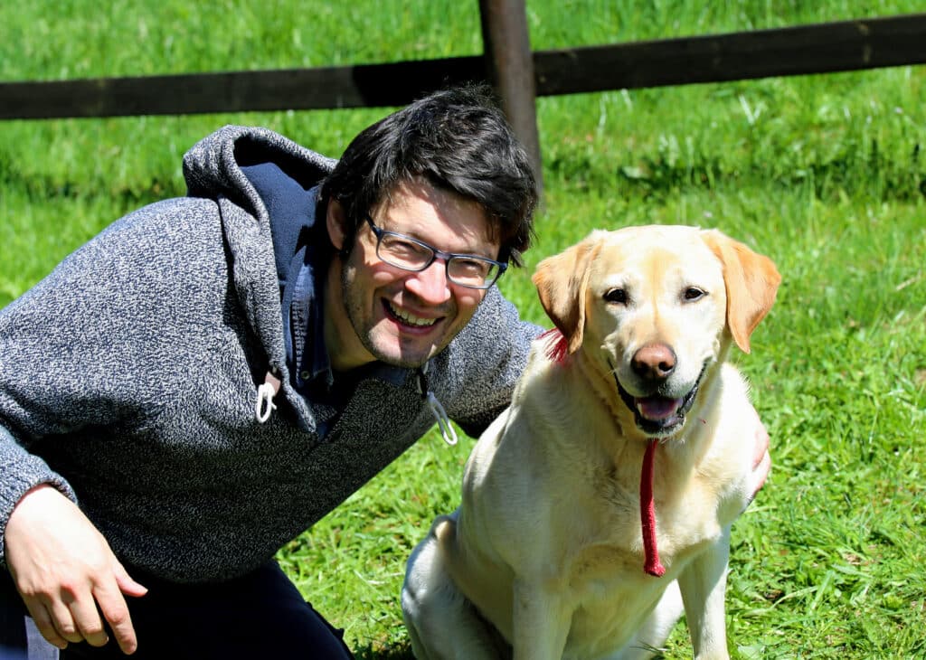 man with black hair smiling with his labrador dog