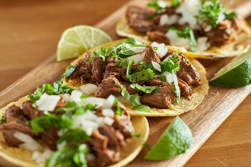 three carne asada mexican street tacos in corn tortilla with lime